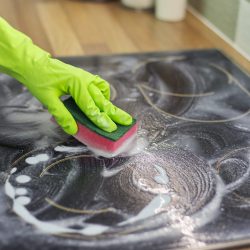 Primer plano de una mano de mujer limpiando una superficie eléctrica de vitrocerámica de cocina moderna con esponja y detergente