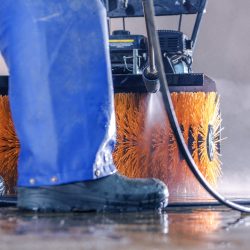 Trabajo de lavado a presión. Una persona limpiando su cepillo industrial con un potente chorro de agua.